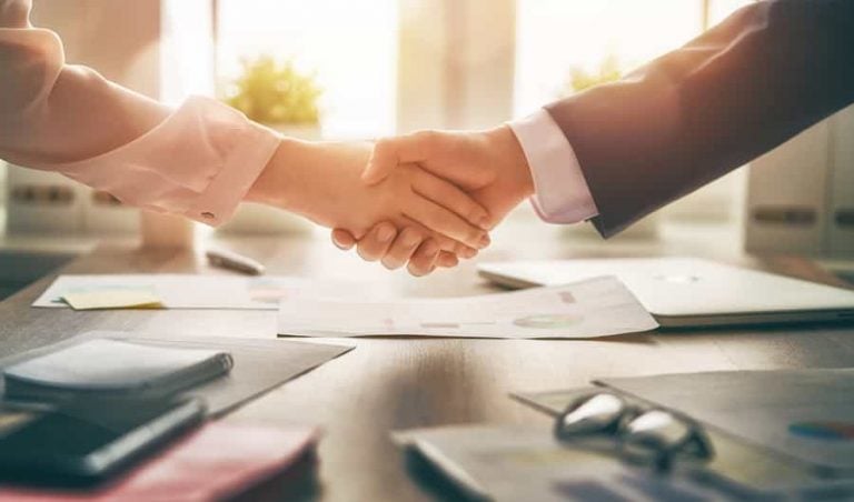 A close up of a handshake with an office in the background