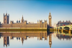 Big Ben and the Houses of Parliament pictured from across the Thames, with the buildings reflected in the calm water 