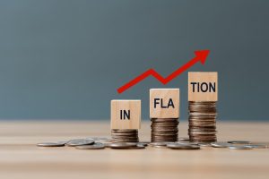 Wooden blocks spelling out the word 'inflation' placed on piles of coins, with a red upwards arrow above