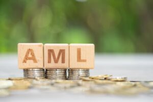 The letters A M L printed on small wooden blocks, which are placed on piles of coins