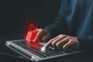 Close-up of hands typing on a laptop with an overlaid graphic of a red warning triangle