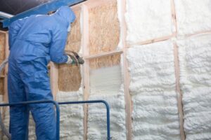 Spray foam being installed in a roof space by a person wearing blue overalls
