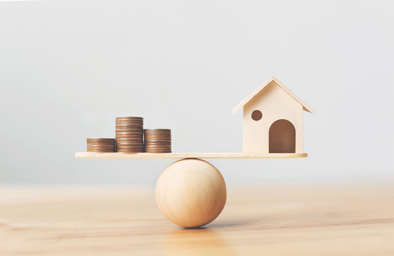 A basic wooden model of a home balanced with a pile of coins on top of a wooden ball