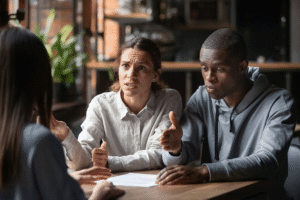 An angry looking couple appear to be having a heated discussion with a professional woman at a desk