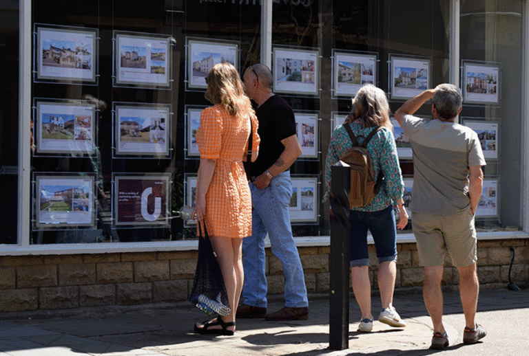 Four people look in an estate agent window on a sunny day