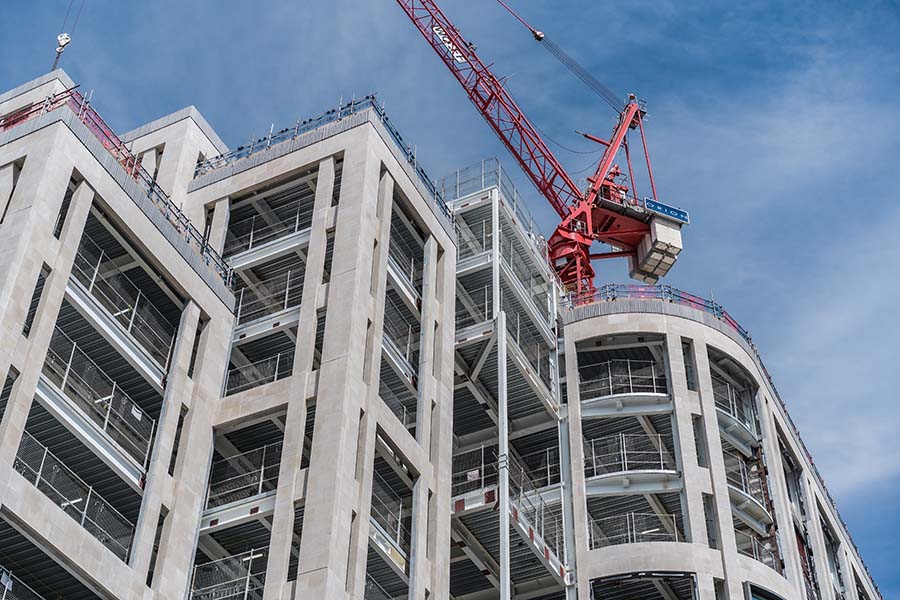 A construction site in London, featuring a large concrete building with visible scaffolding next to a towering red crane.
