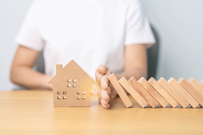 A woman's hand prevents dominos from falling into a small wooden house