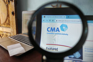 A magnifying glass enhances the CMA logo seen on a laptop screen