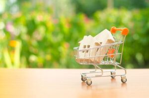 Toy houses in a shopping trolley with sunlit greenery in the background