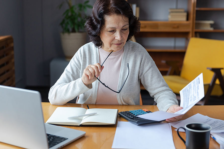 An older lady sits at a desk with a calculator and pile of papers