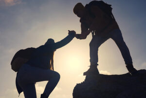 Silhouette of hikers at the top of a mountain, with one helping the other up