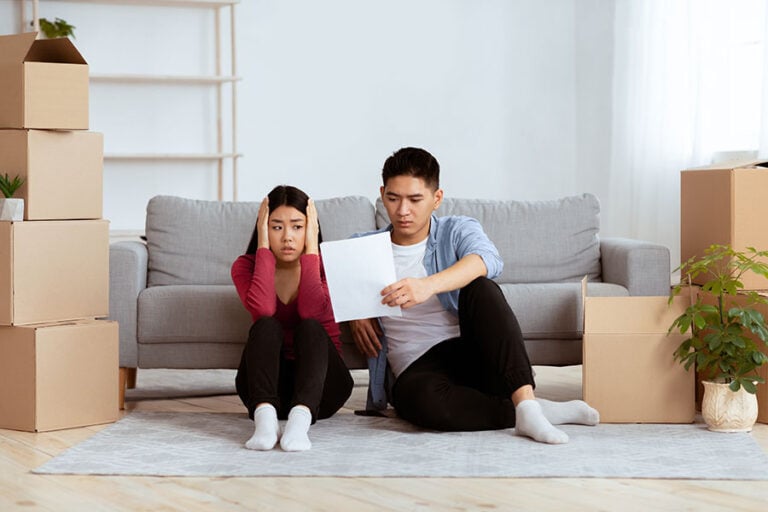 A sad looking couple examine a letter, surrounded by packing boxes