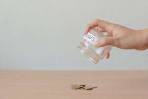 A hand holds a glass jar marked 'savings', which has been tipped upside down to empty a few coins onto a table