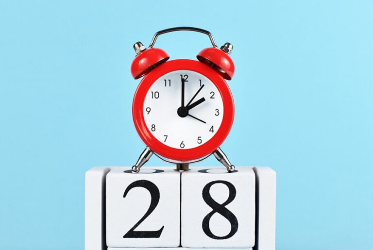A red alarm clock on top of blocks with the number 28 them, against a blue background