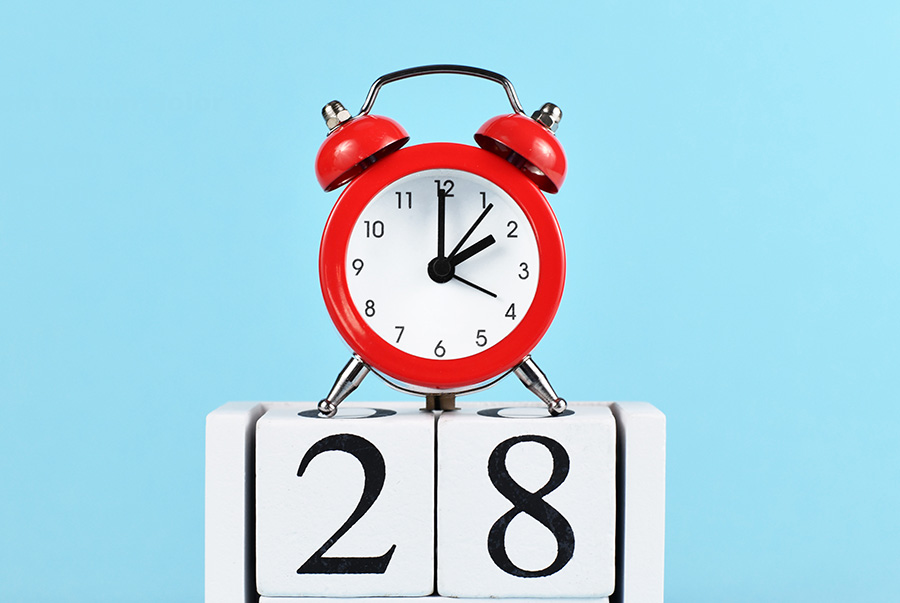 A red alarm clock on top of blocks with the number 28 them, against a blue background