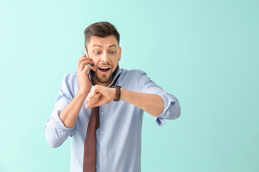 A man looks annoyed while taking a phone call and looking at his watch