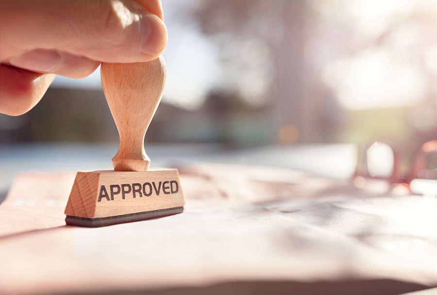 A hand holding an ink stamp with 'approved' written on it