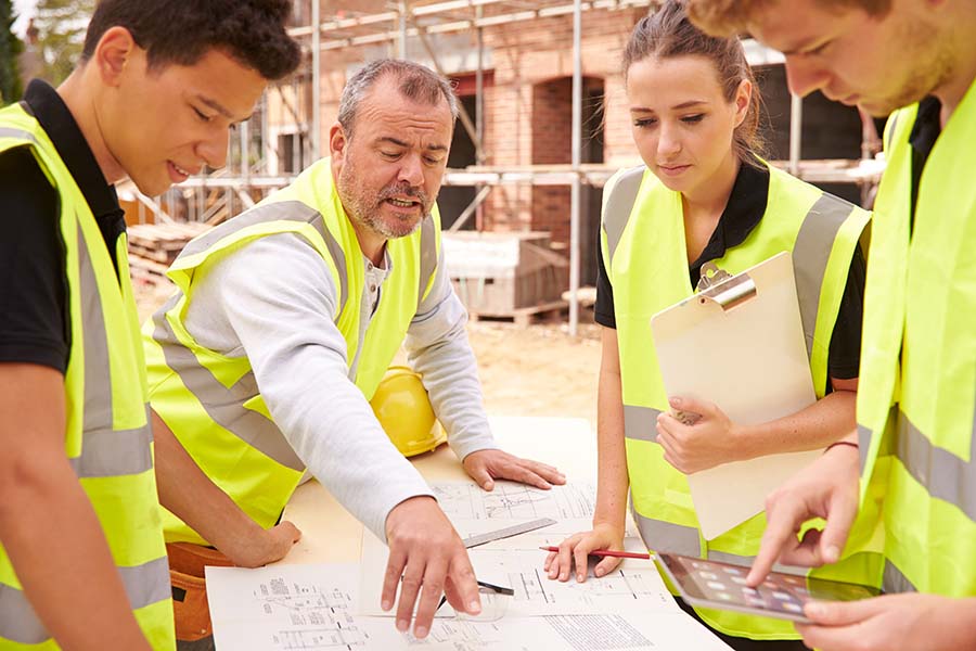 Young building apprentices on site being shown plans by an older worker