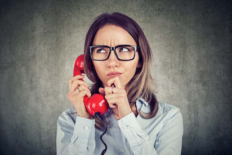 A frustrated looking woman holding an old-fashioned red phone