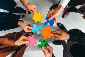 Close up of hands, each holding a coloured piece of a jigsaw