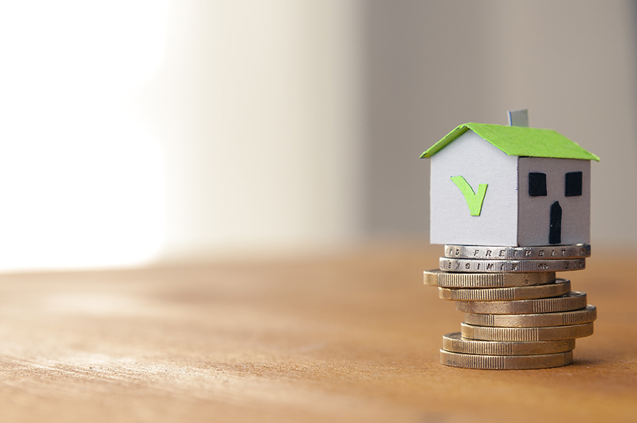 A small toy house with a green tick on the side on top of a pile of coins