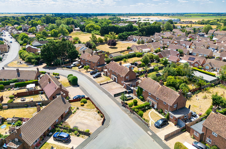 An aerial view of a neighbourhood in England during a drought, with dry yellow lawns and field
