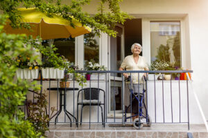 An older lady stands on the plant-filled balcony of a home