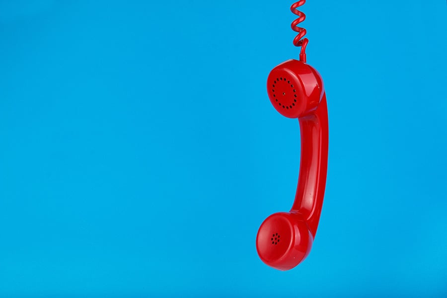 An old-fashioned red phone handset hangs against a blue background, appearing to have been abandoned