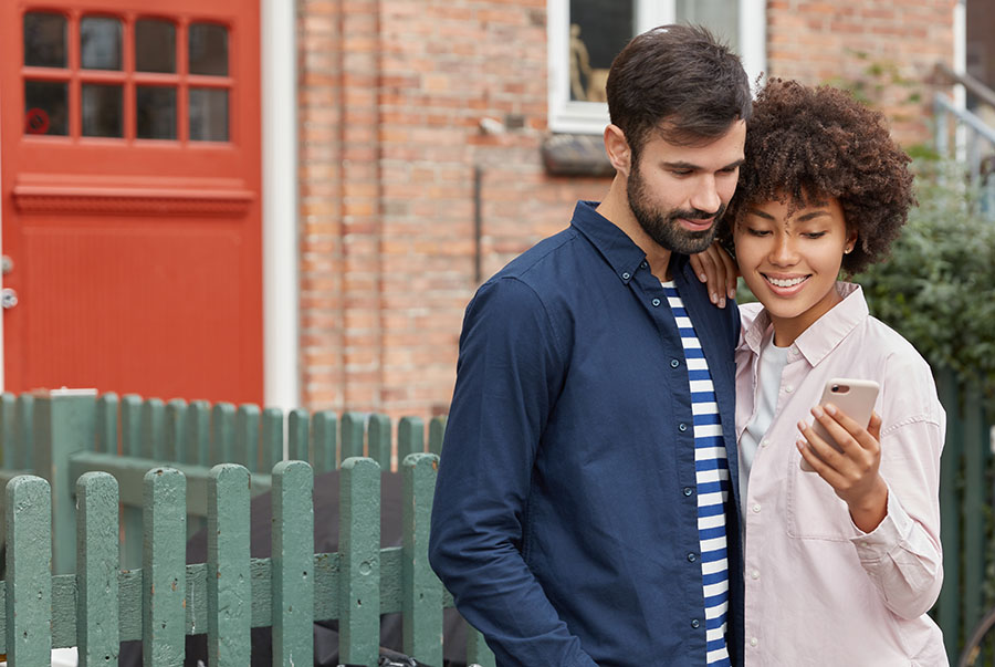 A couple look at their phone while standing outside a house
