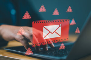 A graphic of a red email symbol surrounded by red warning signs is overlaid across a photo of a laptop keyboard