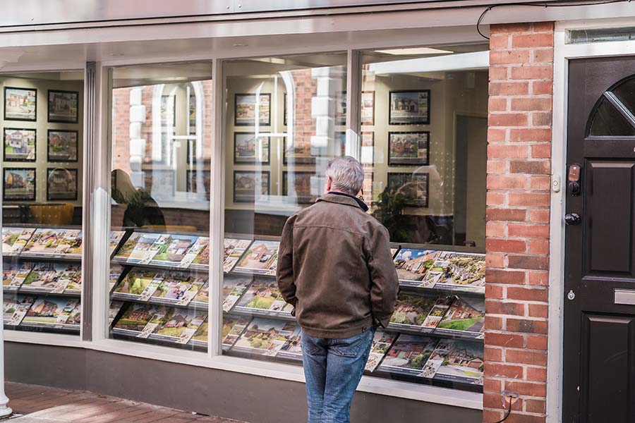An older man looks in the window of an estate agent