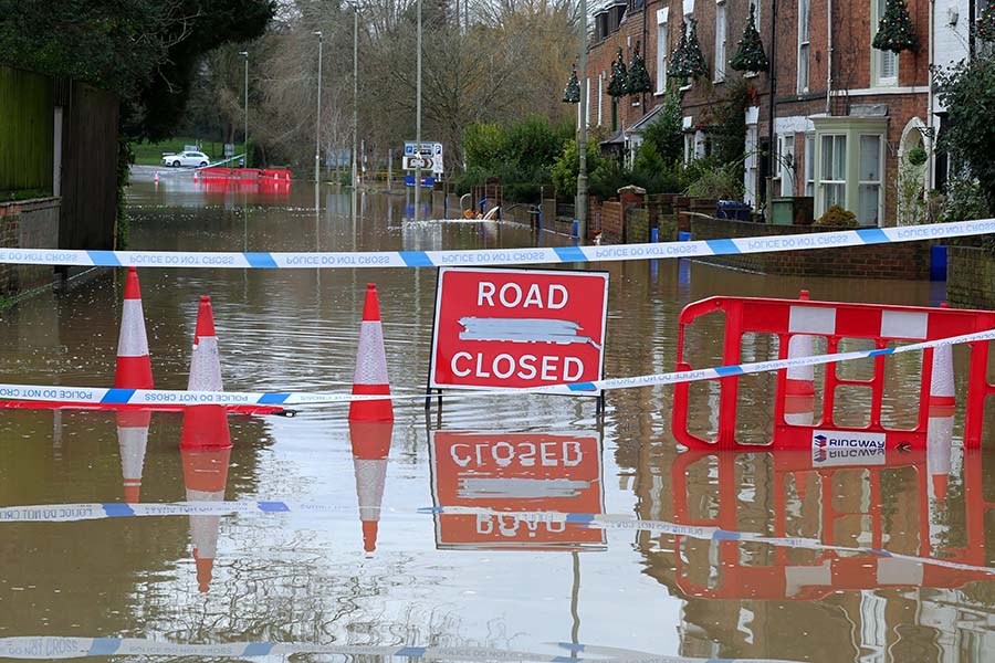 A flooded street is cordoned off with a 'road closed' sign