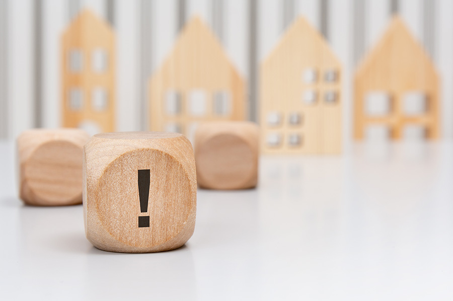Four small wooden models of houses in the background, with a small wooden cube with a black exclamation mark in the foreground