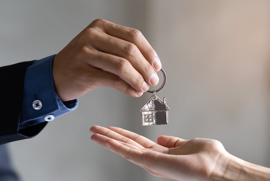 A close up of a keyring in a house shape being passed from one hand to another