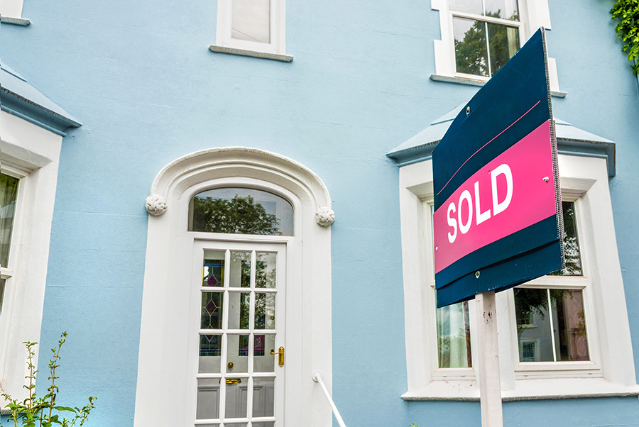 A large house painted pale blue with a sold sign outside