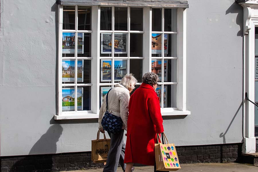 Two older ladies walk past an estate agent's window