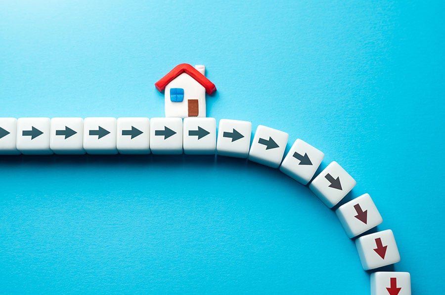 A toy house placed above a row of small white blocks with arrows on them. The row falls downwards as it gets to the end