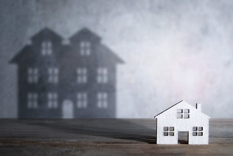 A small model of a house lit from the front to create a large shadow