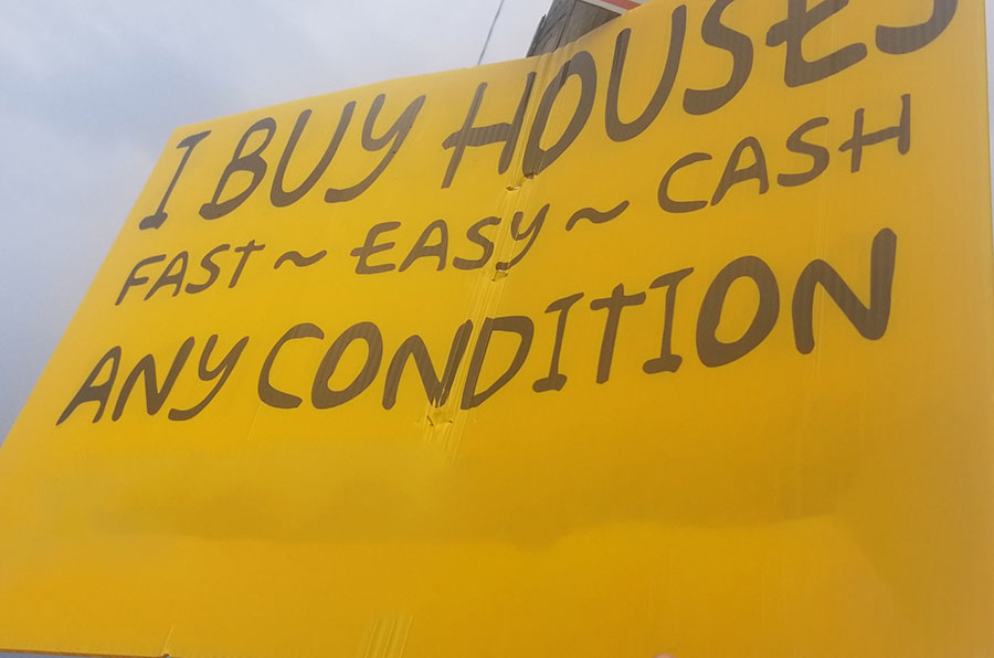 A sign on a lamp post reading 'i buy houses, fast, easy, cash, any condition'