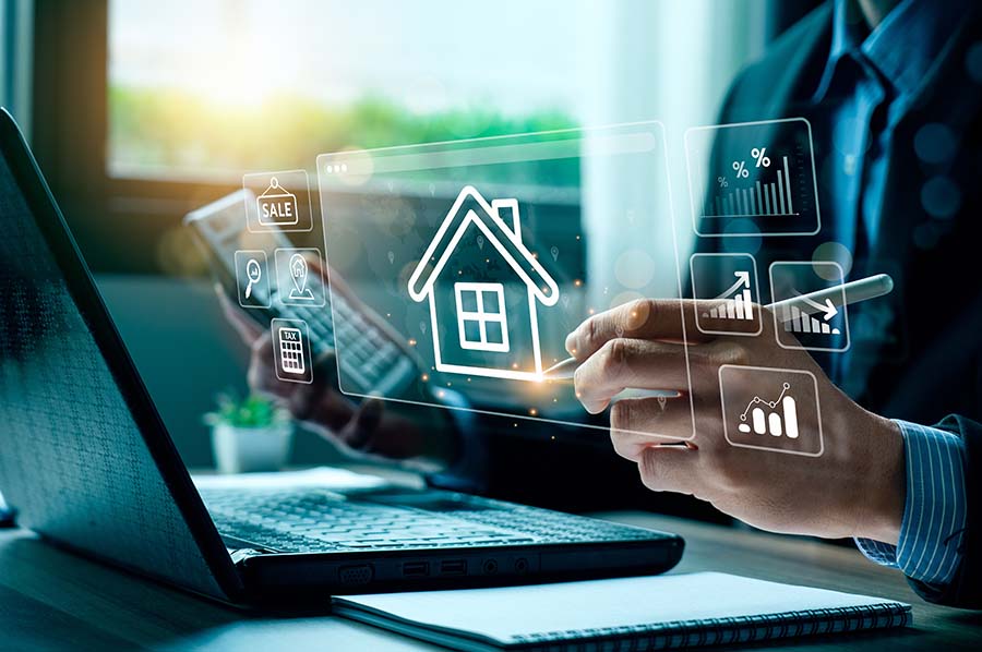 A close up of hands next to a laptop, one hand holding a calculator. The image is overlaid with a graphic of a house, graphs and charts