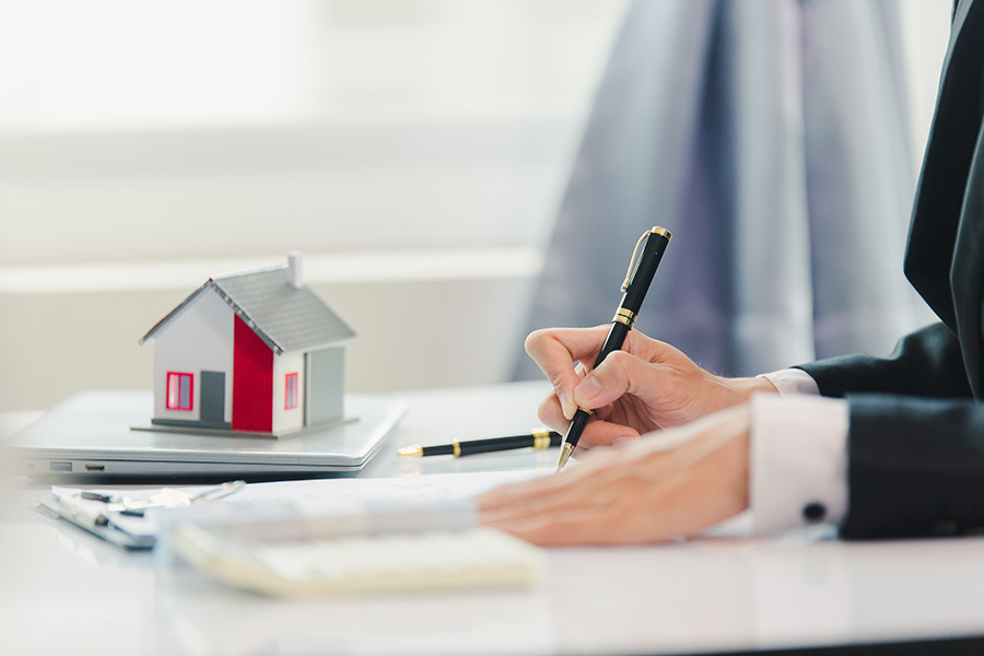 A close-up of a person filling in forms, with a small model house on the desk