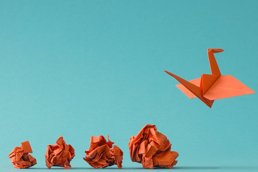 An orange origami bird appears to take flight from four crumpled pieces of orange paper