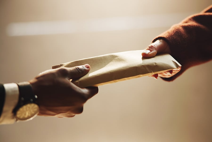 A close up of an envelope seemingly full of cash being handed from one person to another