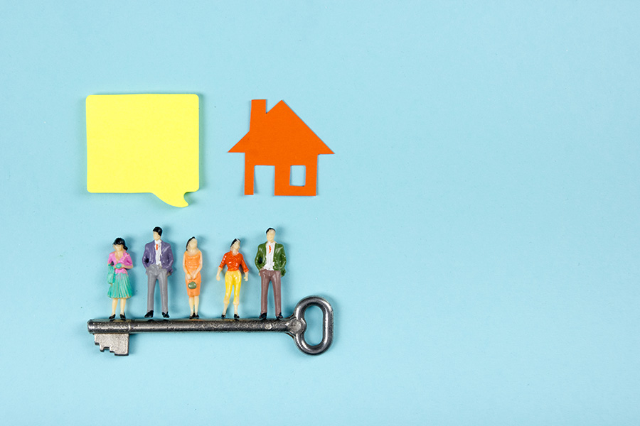 An illustration with five small model figures appearing to be standing on a key, with paper cut outs of a speech bubble and a house above them