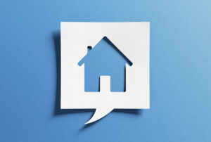 A house shape is cut out of a piece of white paper in the shape of a speech bubble, set against a blue background