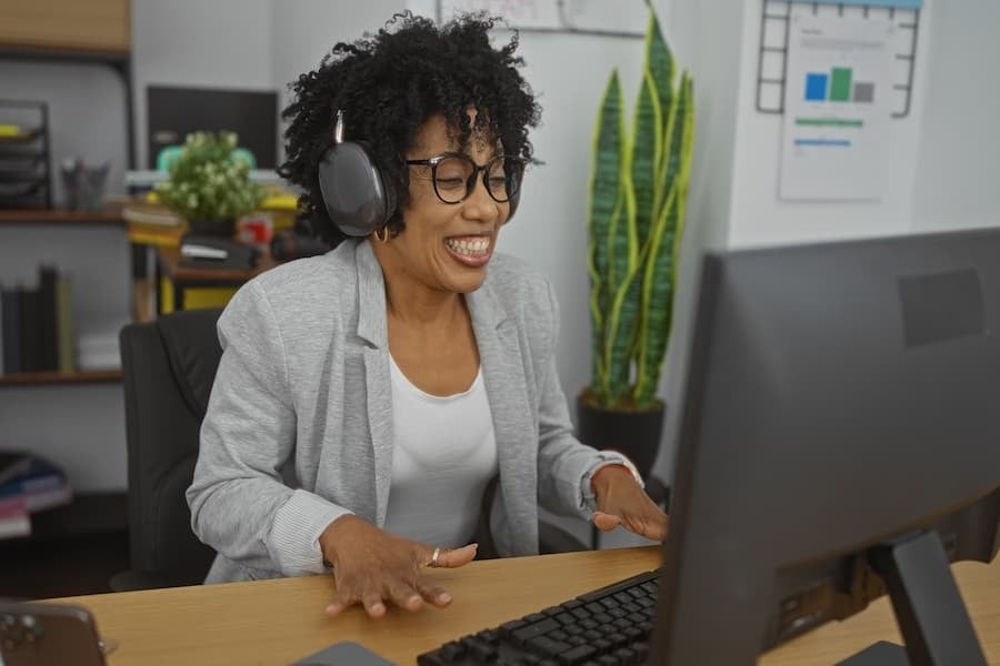 A woman sitting at a desk smiles as she looks at her computer screen