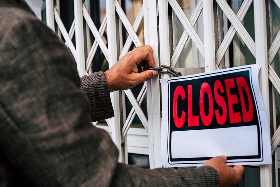 man puts a closed sign across metal shutters closed with a padlock