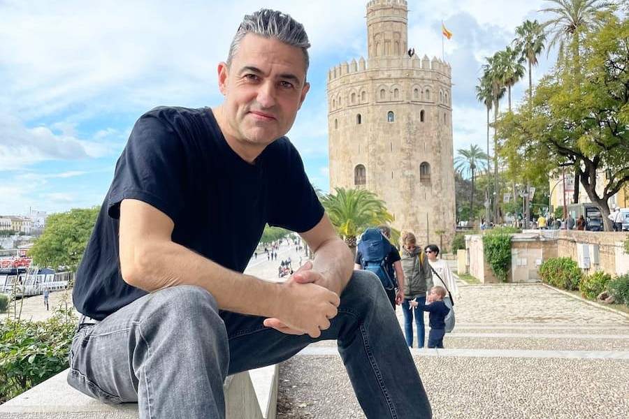 Dan Warburton, host of The Law Firm Owners Podcast, looks relaxed sitting on a low wall in a sunny location, with a historic building in the background