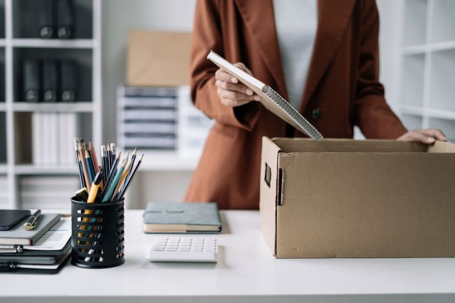 A woman is packing up the contents of her office desk into a cardboard box