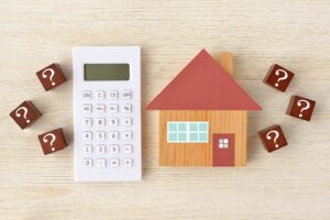 A small wooden house next to a calculator and surrounded by question marks